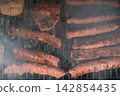 Meat patties and sausage rolls cooking on grill over charcoal. Smoky BBQ scene Meat patties and sausage rolls cooking on grill over charcoal. Smoky BBQ scene 142854435