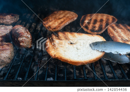 Grilled bread slices over hot coals with tongs Grilled bread slices over hot coals with tongs 142854436