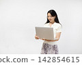 A young Japanese woman is using a laptop in front of a white wall. 142854615