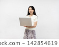 A young Japanese woman smiles at the camera, holding a laptop, in front of a white wall. 142854619