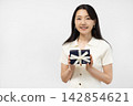 A young Japanese woman smiles at the camera, holding a gift box in front of a white wall. 142854621