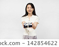 A young Japanese woman smiles at the camera, holding a gift box in front of a white wall. 142854622