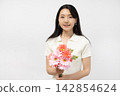 A young Japanese woman smiles at the camera, holding a bouquet of flowers, in front of a white wall. 142854624