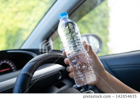 Asian woman driver hold cold water for drink in car, dangerous and risk an accident. Asian woman driver hold cold water for drink in car, dangerous and risk an accident. 142854635