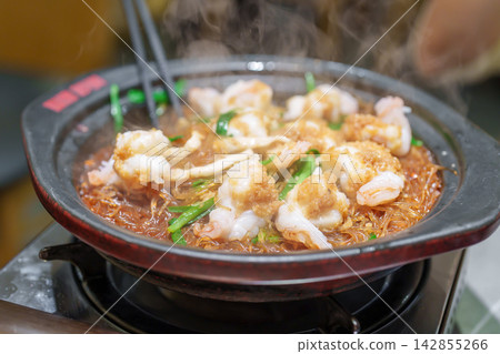 Woman tourist eating baked shrimp with glass noodles and garlic in restaurant. Popular foods for tourist eating in Chengdu, China. Chinese Asia and Sichuan foods concept Woman tourist eating baked shrimp with glass noodles and garlic in restaurant. Popular foods for tourist eating in Chengdu, China. Chinese Asia and Sichuan foods concept 142855266