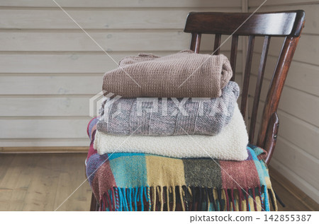 Cozy pile of warm clothes, sweaters on a vintage wooden chair. 142855387