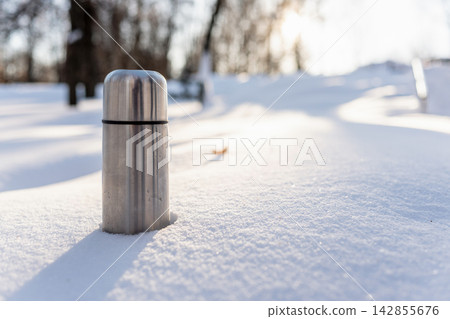 Stainless steel thermos in snowy winter landscape Stainless steel thermos in snowy winter landscape 142855676