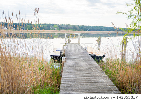 Wooden pier with boats on calm water in Breege on Ruegen island in Germany. Travel, nature and peaceful coastal atmosphere near the Baltic Sea Wooden pier with boats on calm water in Breege on Ruegen island in Germany. Travel, nature and peaceful coastal atmosphere near the Baltic Sea 142855817