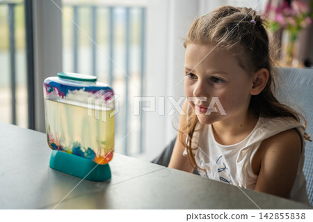 Little girl watching artemia in aquarium as first experience caring for small living creatures. Responsibility, empathy and nurturing behavior concept. 142855838