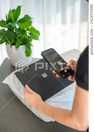Smartphone scanning small QR code on parcel with focus on label for delivery tracking at home. Contactless identification and logistics technology concept. Smartphone scanning small QR code on parcel with focus on label for delivery tracking at home. Contactless identification and logistics technology concept. 142855996