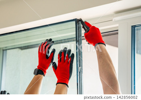 Worker separating triple glazed window glass unit into individual panels for safe handling and disposal after damage in apartment. Window repair, glass recycling and maintenance process concept. Worker separating triple glazed window glass unit into individual panels for safe handling and disposal after damage in apartment. Window repair, glass recycling and maintenance process concept. 142856002