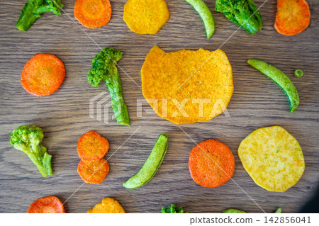 Seamless pattern of vegetable chips with broccoli carrot peas and sweet potato on wooden background. Healthy snack texture and clean eating concept. Seamless pattern of vegetable chips with broccoli carrot peas and sweet potato on wooden background. Healthy snack texture and clean eating concept. 142856041