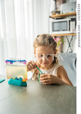 Little girl carefully measuring food for artemia with spoon from packet. Calm focused activity and mindful screen free learning routine concept Little girl carefully measuring food for artemia with spoon from packet. Calm focused activity and mindful screen free learning routine concept 142856104