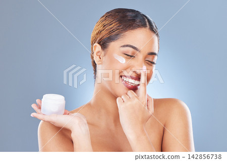 Smile, cream and woman with dermatology, beauty and cosmetics on a blue studio background. Face, person and model with lotion, shine and glow with moisturizer, creme and skincare with aesthetic Smile, cream and woman with dermatology, beauty and cosmetics on a blue studio background. Face, person and model with lotion, shine and glow with moisturizer, creme and skincare with aesthetic 142856738