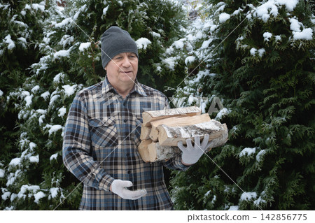 Mature man carrying firewood outdoors in winter Mature man carrying firewood outdoors in winter 142856775