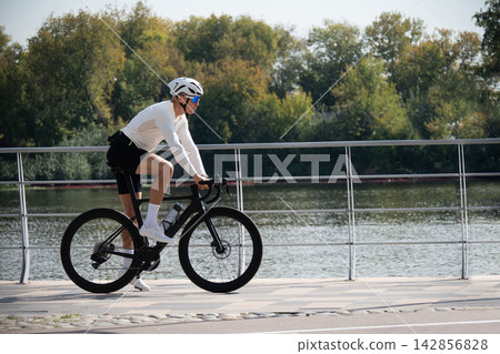 Road cyclist riding bicycle by waterfront 142856828