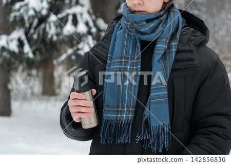 Young man holding thermos in winter park Young man holding thermos in winter park 142856830