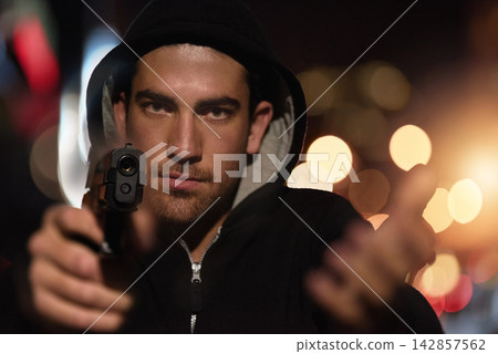 Man, portrait and gun point in city as gangster thief with bokeh lights at night or robbery pistol, hoodie or dark. Male person, face and hand or downtown for dangerous crime or steal, thug or theft Man, portrait and gun point in city as gangster thief with bokeh lights at night or robbery pistol, hoodie or dark. Male person, face and hand or downtown for dangerous crime or steal, thug or theft 142857562