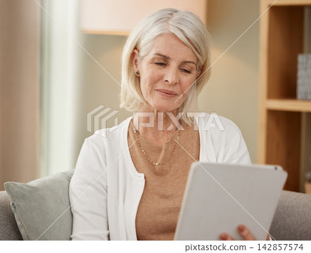 Senior woman, tablet and sofa for reading in house with technology, smile for news on social media. Search, ebook or living room for research on retirement home with care service, online for wellness 142857574