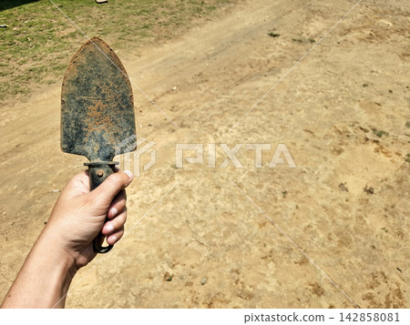 Hand holding small metal trowel tool for gardening outdoors. Hand holding small metal trowel tool for gardening outdoors. 142858081