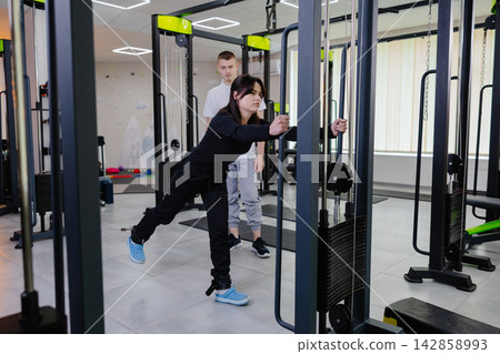 Woman exercising with cable machine and personal trainer assistance Woman exercising with cable machine and personal trainer assistance 142858993