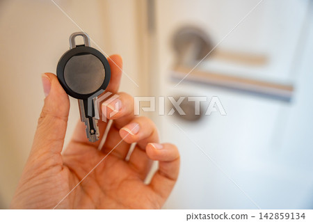 Hand holding an RFID key fob in front of an apartment door with lock and handle. Concept of electronic access control, keyless entry and residential security. Hand holding an RFID key fob in front of an apartment door with lock and handle. Concept of electronic access control, keyless entry and residential security. 142859134