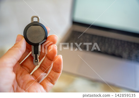 Hand holding an RFID key fob in front of a computer monitor. Concept of programming electronic access credentials, smart security systems and digital access management. Hand holding an RFID key fob in front of a computer monitor. Concept of programming electronic access credentials, smart security systems and digital access management. 142859135