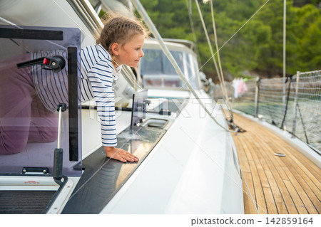 Young girl climbing out of hatch on sailing yacht and looking at camera. Exploring life aboard turns family sailing vacation into playful childhood adventure Young girl climbing out of hatch on sailing yacht and looking at camera. Exploring life aboard turns family sailing vacation into playful childhood adventure 142859164