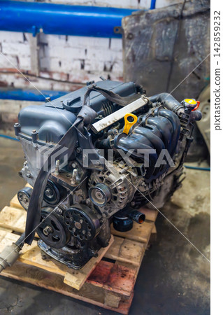 Removed car engine with intake manifold and alternator in auto repair workshop. Dismantled power unit represents engine replacement overhaul and used car repair Removed car engine with intake manifold and alternator in auto repair workshop. Dismantled power unit represents engine replacement overhaul and used car repair 142859232
