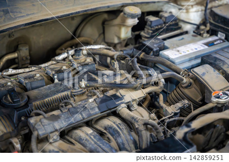 Dusty engine compartment of a used car with battery hoses and wiring. Vehicle condition represents inspection maintenance and repair of a pre owned automobile Dusty engine compartment of a used car with battery hoses and wiring. Vehicle condition represents inspection maintenance and repair of a pre owned automobile 142859251