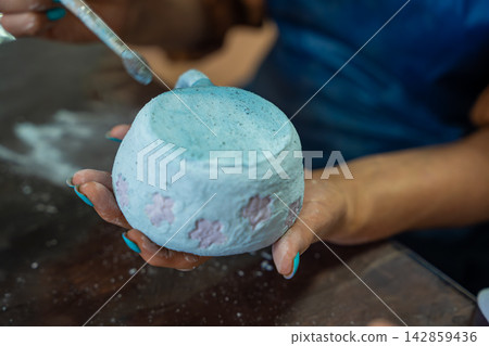 Hands applying glaze to outer surface of handmade ceramic mug with brush. Close up pottery glazing process represents craftsmanship and handmade ceramic production 142859436