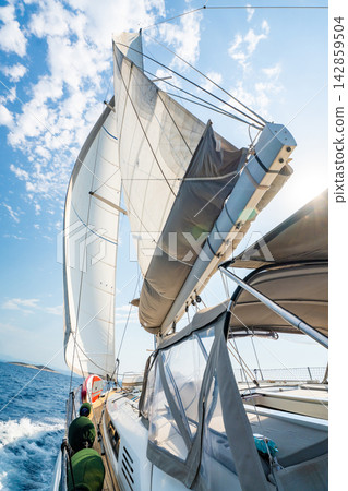 View from deck of sailing yacht with fully deployed sails cruising across Adriatic Sea under bright blue sky. Dynamic maritime travel scene representing freedom, adventure and nautical lifestyle View from deck of sailing yacht with fully deployed sails cruising across Adriatic Sea under bright blue sky. Dynamic maritime travel scene representing freedom, adventure and nautical lifestyle 142859504