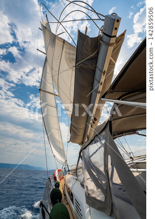 Low angle view of sailing yacht with fully deployed sails, taut rigging and windblown lines while cruising across Adriatic Sea. Dynamic maritime scene highlighting wind power, seamanship and freedom. 142859506
