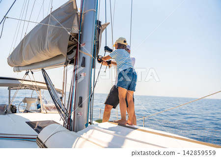 Father supervising his daughter while learning sailing skills on a family yacht. Building independence, confidence, responsibility and teamwork through real sailing experience. 142859559