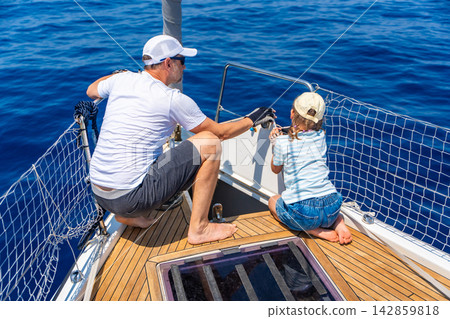Father teaching his daughter basic yacht maintenance during a family sailing trip. Learning practical sailing skills, teamwork and confidence through shared outdoor experience. Father teaching his daughter basic yacht maintenance during a family sailing trip. Learning practical sailing skills, teamwork and confidence through shared outdoor experience. 142859818
