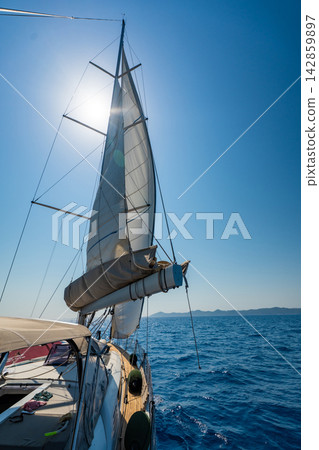 Mainsail on a sailing yacht while cruising across the sea under a clear blue sky. Concept of wind power, sailing, navigation, freedom and life aboard. Mainsail on a sailing yacht while cruising across the sea under a clear blue sky. Concept of wind power, sailing, navigation, freedom and life aboard. 142859897
