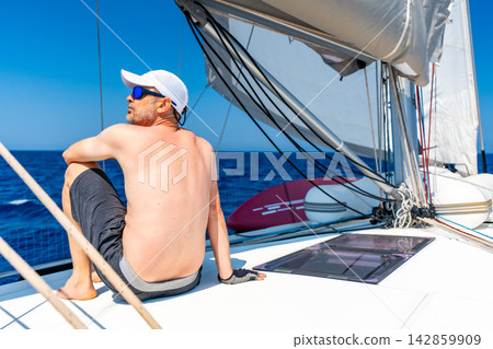 Man relaxing on a sailing yacht during an offshore voyage. Peaceful lifestyle and freedom while living at sea. Man relaxing on a sailing yacht during an offshore voyage. Peaceful lifestyle and freedom while living at sea. 142859909