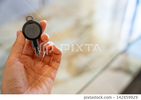 Hand holding an RFID key fob with electronic access chip inside a modern apartment. Concept of smart access control, keyless entry and residential security. Hand holding an RFID key fob with electronic access chip inside a modern apartment. Concept of smart access control, keyless entry and residential security. 142859929