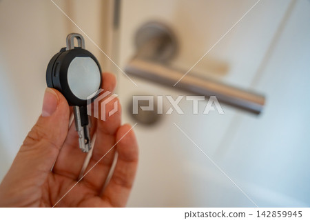 Hand holding an RFID key fob in front of an apartment door with lock and handle. Concept of electronic access control, keyless entry and residential security. Hand holding an RFID key fob in front of an apartment door with lock and handle. Concept of electronic access control, keyless entry and residential security. 142859945