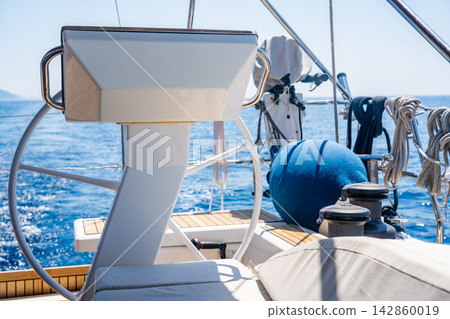 View of the helm station, steering wheel and cockpit of a modern sailing yacht cruising on the open sea. Concept of yacht navigation, sailing, seamanship, marine technology and luxury boating. View of the helm station, steering wheel and cockpit of a modern sailing yacht cruising on the open sea. Concept of yacht navigation, sailing, seamanship, marine technology and luxury boating. 142860019