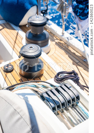 Sailboat winches and rope clutches on the deck of a modern sailing yacht. Professional sailing equipment for sail handling and boat control. Sailboat winches and rope clutches on the deck of a modern sailing yacht. Professional sailing equipment for sail handling and boat control. 142860023