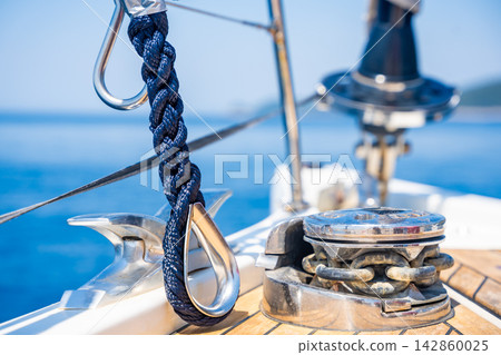 Mooring rope secured to a stainless steel cleat on the deck of a modern sailing yacht. Safe docking equipment and seamanship concept. Mooring rope secured to a stainless steel cleat on the deck of a modern sailing yacht. Safe docking equipment and seamanship concept. 142860025