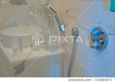 Modern walk in shower with glass partition, handheld showerhead and marble wall tiles. Contemporary bathroom design, hygiene and comfortable daily living. Modern walk in shower with glass partition, handheld showerhead and marble wall tiles. Contemporary bathroom design, hygiene and comfortable daily living. 142860071