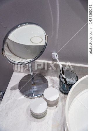 Minimalist bathroom countertop with a single toothbrush, mirror and skincare containers. Bachelor lifestyle, solo living and modern everyday routine. Minimalist bathroom countertop with a single toothbrush, mirror and skincare containers. Bachelor lifestyle, solo living and modern everyday routine. 142860081