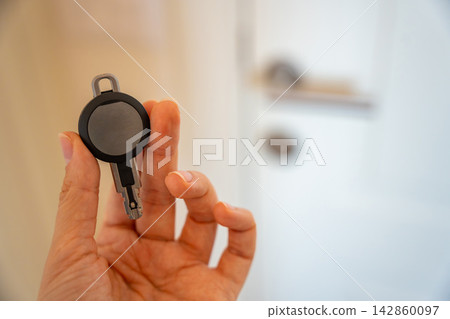 Hand holding an RFID key fob in front of an apartment door with lock and handle. Concept of electronic access control, keyless entry and residential security. Hand holding an RFID key fob in front of an apartment door with lock and handle. Concept of electronic access control, keyless entry and residential security. 142860097