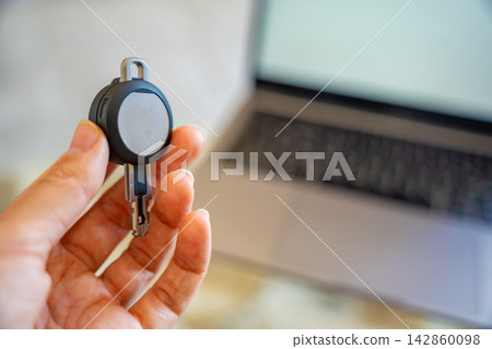 Hand holding an RFID key fob in front of a computer monitor. Concept of programming electronic access credentials, smart security systems and digital access management. Hand holding an RFID key fob in front of a computer monitor. Concept of programming electronic access credentials, smart security systems and digital access management. 142860098