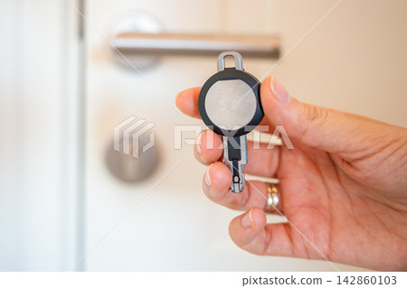 Hand holding an RFID key fob in front of an apartment door with lock and handle. Concept of electronic access control, keyless entry and residential security. Hand holding an RFID key fob in front of an apartment door with lock and handle. Concept of electronic access control, keyless entry and residential security. 142860103