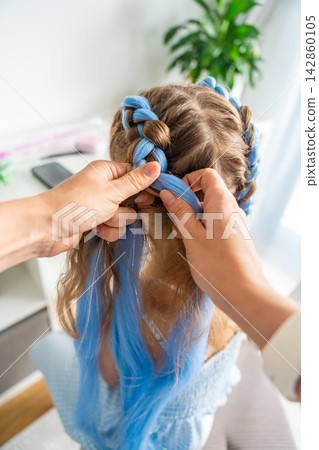 Mother braiding colorful synthetic hair extensions into a young girls hairstyle at home. Creative self expression reflects childhood individuality fashion trends and Generation Alpha style Mother braiding colorful synthetic hair extensions into a young girls hairstyle at home. Creative self expression reflects childhood individuality fashion trends and Generation Alpha style 142860105