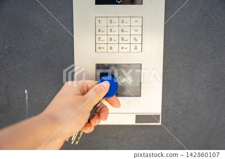 Person using contactless key fob on residential building access control system. Secure entry technology supports convenient and controlled property access Person using contactless key fob on residential building access control system. Secure entry technology supports convenient and controlled property access 142860107
