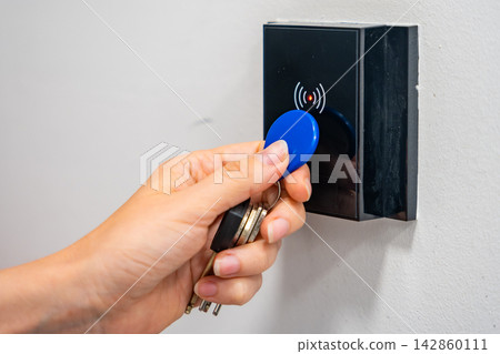 Person using contactless key fob on indoor access control reader. Secure building access protects restricted areas and residential facilities Person using contactless key fob on indoor access control reader. Secure building access protects restricted areas and residential facilities 142860111